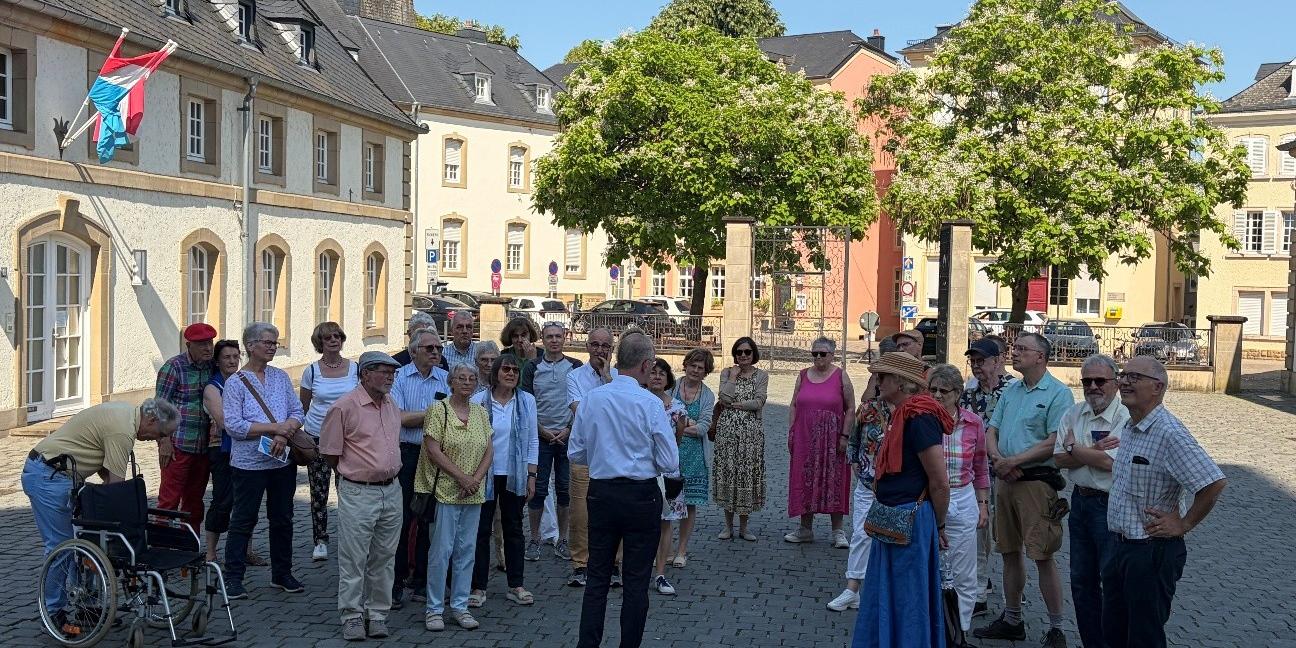 Rektor Erasmy stellt im Schatten der Echternacher Basilika die Architektur vor. Eine Gruppe Teilnehmer hört aufmerksam zu. (c) Katharina Zey-Wortmann Rektor Erasmy stellt im Schatten der Echternacher Basilika die Architektur vor. Eine Gruppe Teilnehmer hört aufmerksam zu.