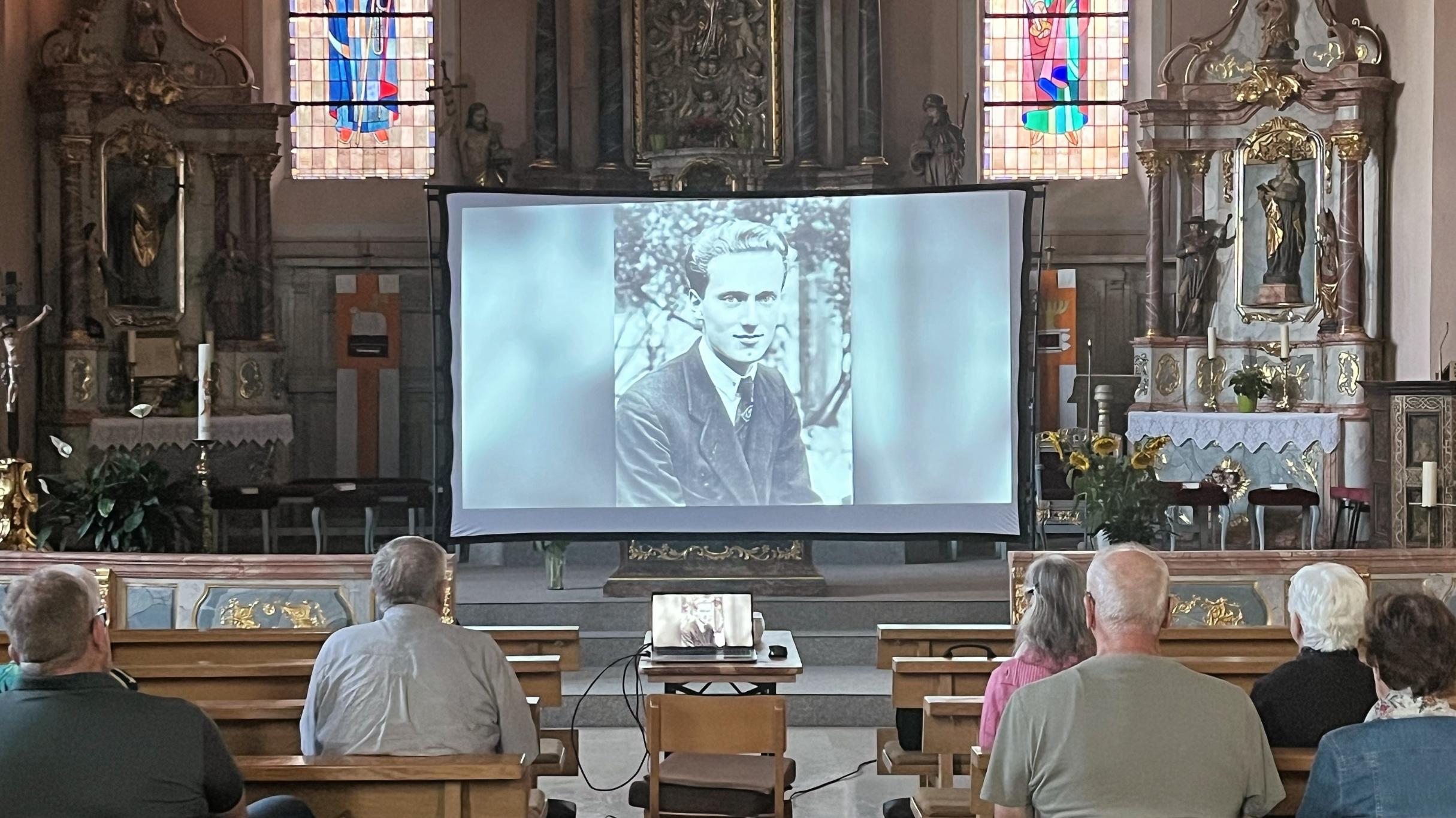 In einer Kirche ist eine Leinwand aufgebaut und Menschen schauen einen Film