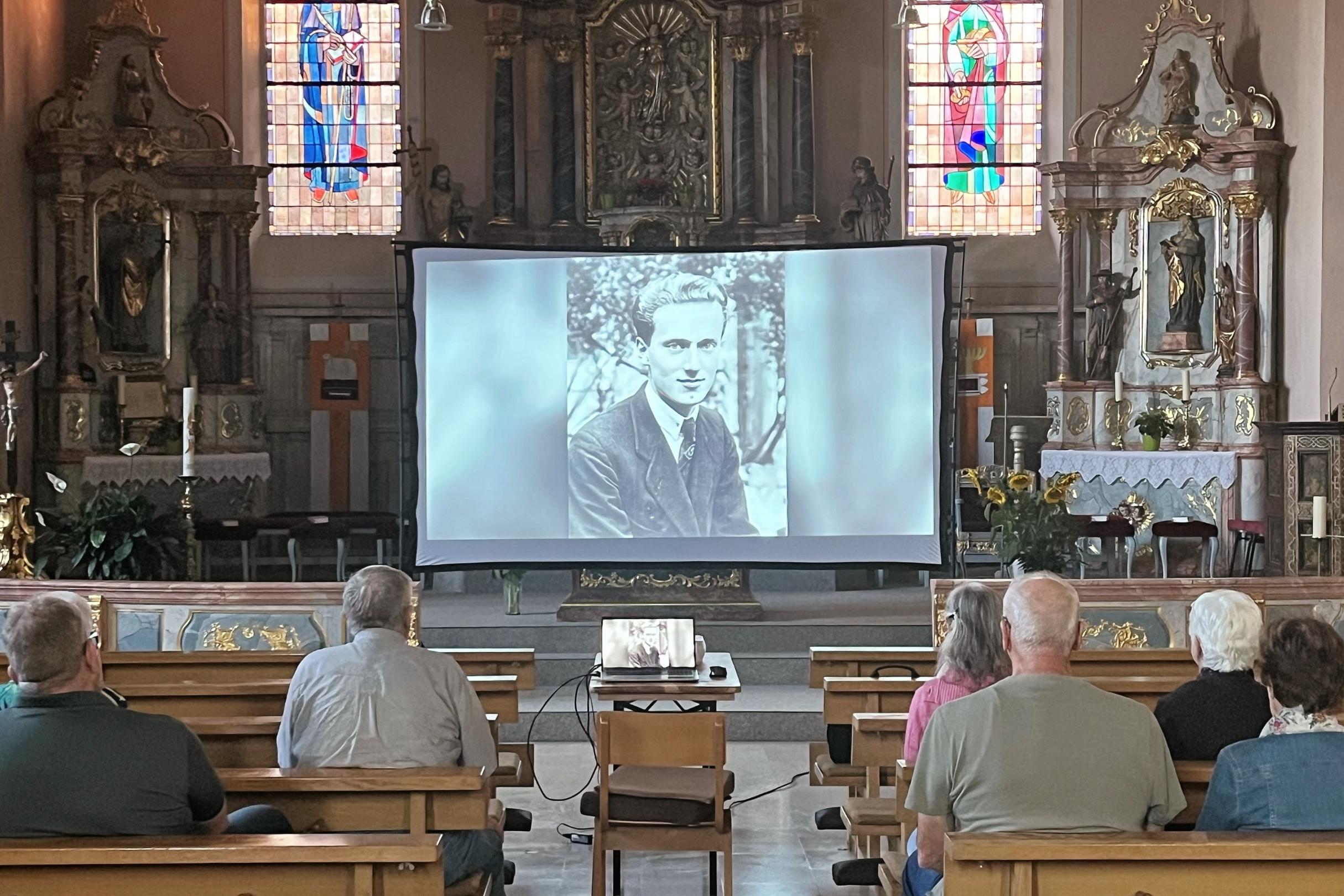 In einer Kirche ist eine Leinwand aufgebaut und Menschen schauen einen Film