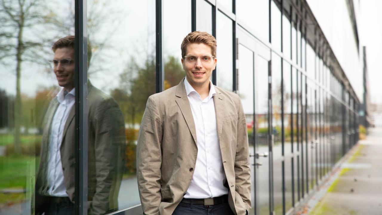 Professor Marten Risius steht vor einem Gebäude mit Glasfront.