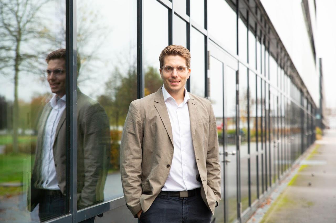 Professor Marten Risius steht vor einem Gebäude mit Glasfront.
