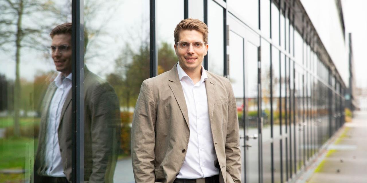 Professor Marten Risius steht vor einem Gebäude mit Glasfront.